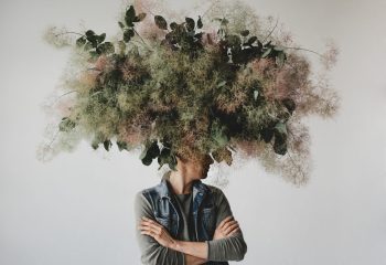Large decorative bouquet made of green leaves and moss hangs over man's head